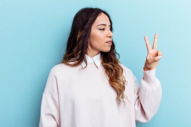 Mavi arka planda izole edilmiş genç Meksikalı kadın neşeli ve tasasız parmakları olan bir barış sembolü gösteriyor..