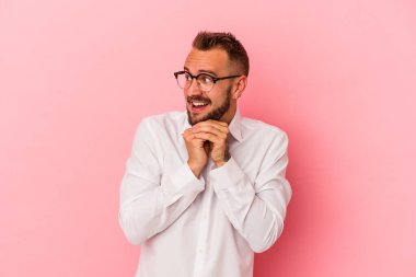 Pembe arka planda izole edilmiş beyaz dövmeli genç bir adam şans için dua ediyor, şaşırıyor ve ağzını açıyor..