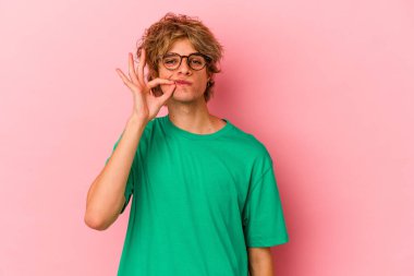 Pembe arka planda izole edilmiş beyaz makyajlı genç bir adam. Parmakları dudaklarında bir sır saklıyor..