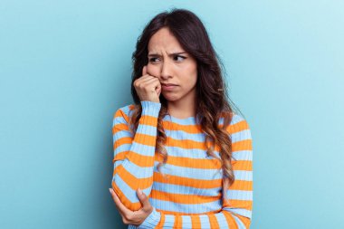 Mavi arka planda izole edilmiş genç Meksikalı kadın üzgün ve düşünceli, fotokopi alanına bakıyor..