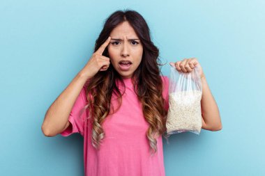 Mavi arka planda yulaf ezmesi tutan genç melez kadın işaret parmağıyla yaptığı hayal kırıklığını gösteriyor..