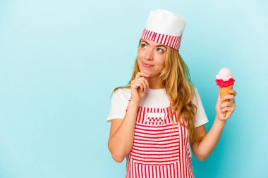 Kafkasyalı dondurma üreticisi kadın elinde dondurma tutarken mavi arka planda izole edilmiş şüpheli ve şüpheci bir ifadeyle yana bakıyor..