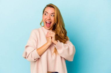 Mavi arka planda izole edilmiş beyaz kadın ellerini çenesinin altında tutuyor, mutlu bir şekilde yana bakıyor..