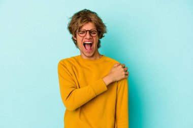 Makyajlı, mavi arka planda, omuz ağrısı çeken genç, beyaz bir adam..