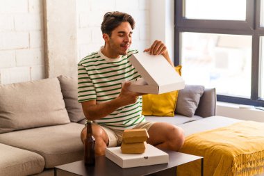 Genç melez adam pizza yiyor, burger yiyor ve bira içiyor.