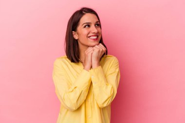 Pembe arka planda izole edilmiş genç beyaz kadın ellerini çenesinin altında tutuyor, mutlu bir şekilde yana bakıyor..