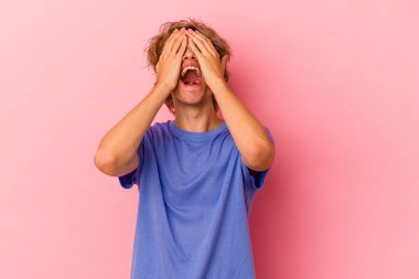 Pembe arka planda soyutlanmış beyaz makyajlı genç bir adam mutlu bir şekilde ellerini başının üstünde tutarak gülüyor. Mutluluk kavramı.