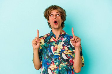 Makyajlı, mavi arka planda izole edilmiş, ağzı açık, üst tarafı gösteren yaz kıyafetleri giyen beyaz bir genç..