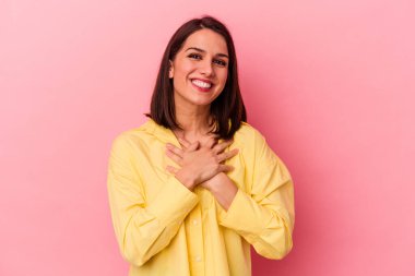 Pembe arka planda soyutlanmış beyaz bir kadın gülüyor, elini yüreğine koyuyor, mutluluk kavramını koruyor..