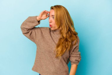 Kafkasyalı kadın mavi arka planda izole edilmiş. Uzağa bakıyor, elini alnına koyuyor..