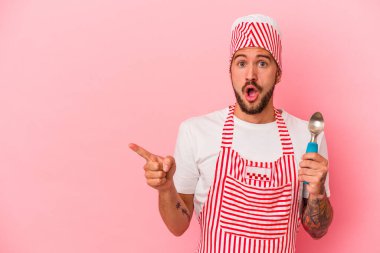 Pembe arka planda izole edilmiş, elinde kaşık tutan dövmeli beyaz bir buz üreticisi var.