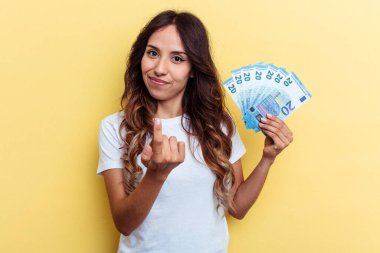 Sarı arka planda izole edilmiş banknotları tutan genç ve melez bir kadın sanki seni davet ediyormuş gibi seni işaret ediyor..