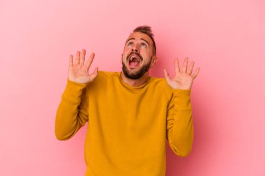 Pembe arka planda izole edilmiş dövmeleri olan genç beyaz bir adam gökyüzüne haykırıyor, yukarı bakıyor ve hayal kırıklığına uğruyor..