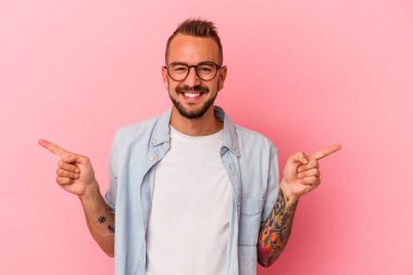 Pembe arka planda dövmeleri olan beyaz genç bir adam farklı fotokopi alanlarını gösteriyor, birini seçiyor, parmaklarıyla gösteriyor..