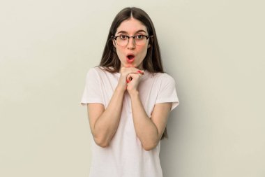 Beyaz tenli genç bir kadın sarı arka planda izole edilmiş şans diliyor, şaşırmış ve ağzını açıp önüne bakıyor..