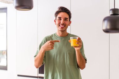 Genç melez adam mutfağında portakal suyu içiyor.