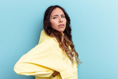 Mavi arka planda izole edilmiş, sırt ağrısı çeken genç Meksikalı kadın..