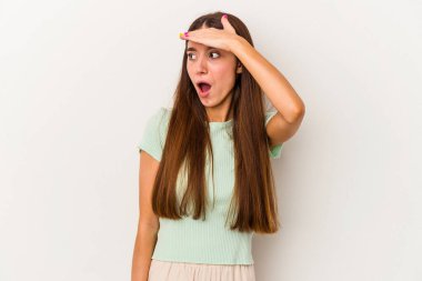 Beyaz arka planda soyutlanmış genç beyaz bir kadın çok uzaklara bakıyor ve elini alnına koyuyor..