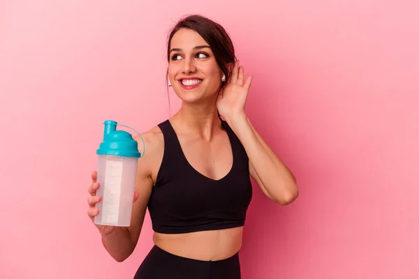 ピンクの背景に隔離されたタンパク質を飲んでいる若い白人女性はゴシップを聞いてみる — ストック写真