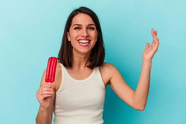 青い背景に隔離されたアイスクリームを手にした若い白人女性は驚き 興奮し 手を上げる — ストック写真
