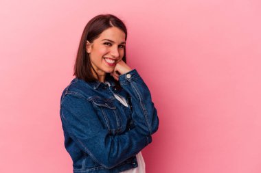 Pembe arka planda izole edilmiş genç beyaz kadın gülümsüyor ve kendinden emin, elleriyle çenesine dokunuyor..