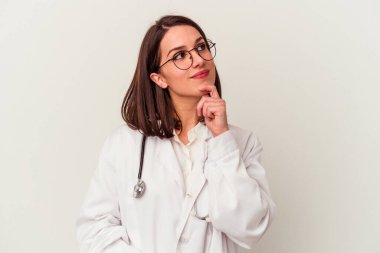 Beyaz arka planda izole edilmiş genç bir doktor şüpheli ve şüpheci bir ifadeyle yana bakıyor..