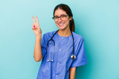 Kafkasyalı genç hemşire mavi arka planda izole edilmiş neşeli ve tasasız parmakları olan bir barış sembolü gösteriyor..