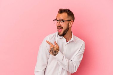 Pembe arka planda dövmeleri olan beyaz bir adam gülümseyen, neşeli ve keyifli bir tarafa bakıyor..