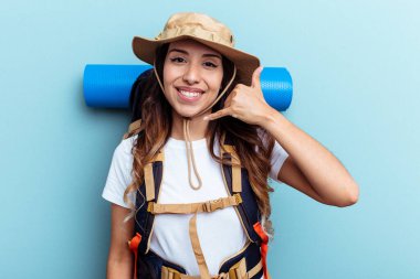 Genç yürüyüşçü melez kadın, mavi arka planda izole edilmiş, parmakları olan bir cep telefonu hareketi gösteriyor..