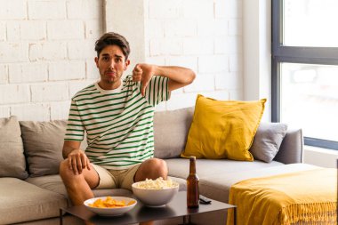 Genç melez adam kanepede oturmuş patlamış mısır yiyor ve hoş olmayan bir jest yapıyor. Anlaşmazlık konsepti.