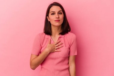 Pembe arka planda izole edilmiş genç beyaz kadın yemin ediyor, elini göğsüne koyuyor..