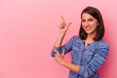 Pembe arka planda izole edilmiş genç beyaz kadın işaret parmaklarıyla işaret ederek heyecanlanıyor..