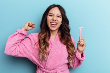 Bornoz giyen genç Meksikalı kadın mavi arka planda izole edilmiş bir bıçak tutuyor zafer kazandıktan sonra yumruğunu kaldırıyor, kazanan konsept..