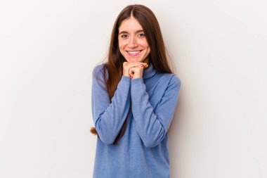 Beyaz arka planda izole edilmiş genç beyaz kadın ellerini çenesinin altında tutuyor, mutlu bir şekilde yana bakıyor..