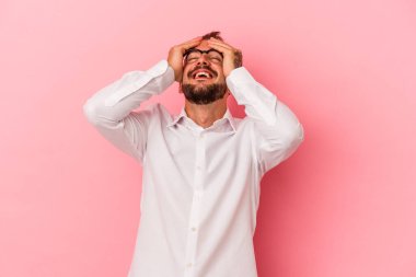 Pembe arka planda izole edilmiş dövmeleri olan beyaz bir genç ellerini başının üstünde tutarak gülüyor. Mutluluk kavramı.