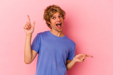 Makyajlı beyaz bir adam pembe arka planda izole edilmiş farklı fotokopi alanlarını gösteriyor, birini seçiyor, parmağıyla gösteriyor..