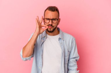 Pembe arka planda dövmeleri olan genç beyaz bir adam. Parmakları dudaklarında bir sır saklıyor..