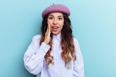 Mavi arka planda izole edilmiş genç Meksikalı kadın yüksek sesle bağırıyor, gözlerini açık ve ellerini gergin tutuyor..