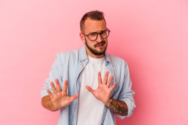 Pembe arka planda dövmeleri olan beyaz bir genç adam tiksinti belirtisi gösteren birini reddediyor..