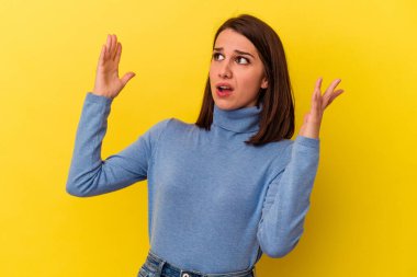 Sarı arka planda izole edilmiş genç beyaz kadın gökyüzüne haykırıyor, yukarı bakıyor, hayal kırıklığına uğramış..