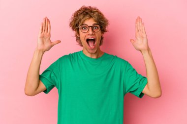 Pembe arka planda soyutlanmış beyaz makyajlı genç bir adam hoş bir sürpriz alıyor, heyecanlı ve el kaldırıyor..