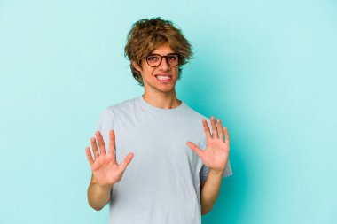 Mavi arka planda soyutlanmış beyaz makyajlı genç bir adam tiksinti belirtisi gösteren birini reddediyor..