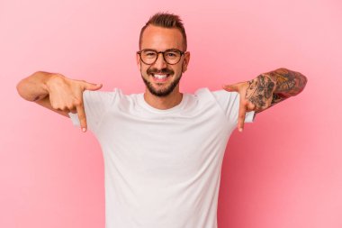 Pembe arka planda izole edilmiş dövmeleri olan beyaz bir genç. Parmakları aşağıda, olumlu hisler içinde..