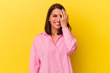 Sarı arka planda izole edilmiş genç beyaz kadın yüzünün yarısını palmiye ile örterek eğleniyor..