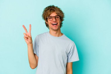 Mavi arka planda soyutlanmış beyaz makyajlı genç bir adam neşeli ve kaygısız parmaklarıyla barış sembolü gösteriyor..