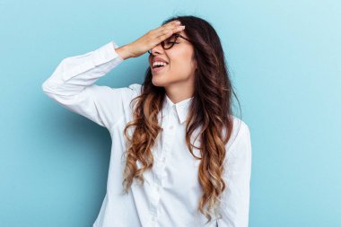 Mavi arka planda izole edilmiş genç Meksikalı kadın elleriyle gözlerini kapatıyor, gülümseyerek bir sürpriz bekliyor..