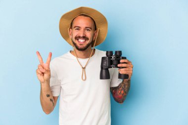 Mavi arka planda iki numaranın parmakları olduğunu gösteren dürbünlü dövmeleri olan genç beyaz bir adam..