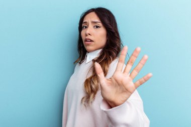 Mavi arka planda izole edilmiş genç Meksikalı kadın, yakın bir tehlike nedeniyle şoka uğruyor.