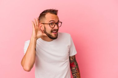 Pembe arka planda izole edilmiş dövmeleri olan beyaz bir adam bir dedikoduyu dinlemeye çalışıyor..