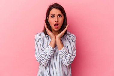 Pembe arka planda izole edilmiş genç beyaz kadın şaşırmış ve şok olmuş..